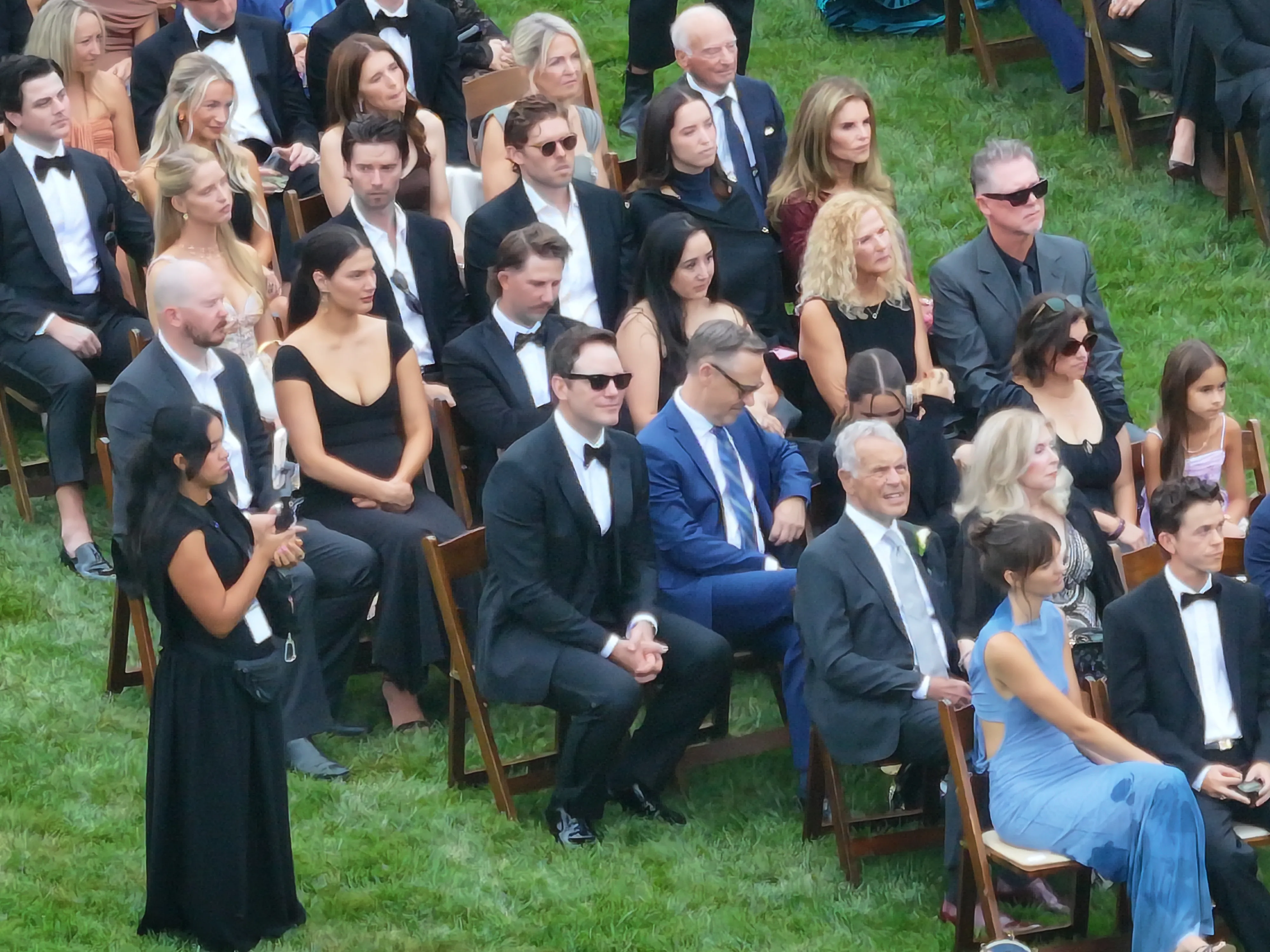 High-angle view of guests, including Rob Lowe, Gwyneth Paltrow, Cameron Diaz, Katy Perry, Chris Pratt, Katherine Schwarzenegger, Maria Shriver, Zoe Saldaña, Adam Levine, and Behati Prinsloo, seated in rows on the grass at an outdoor wedding.