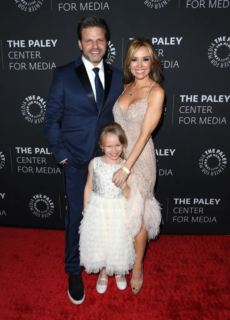 Matthew Miele and Sara Gore posing with a young girl on a red carpet in front of a branded backdrop.