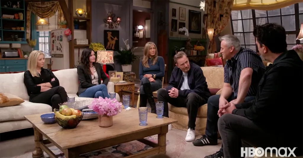 Matthew Perry and the cast of Friends reunite, sitting on couches in a living room set.
