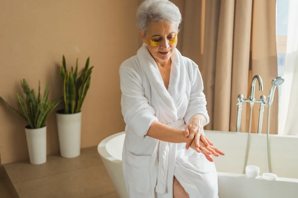 A mature woman applies moisturizing body lotion to her hands.