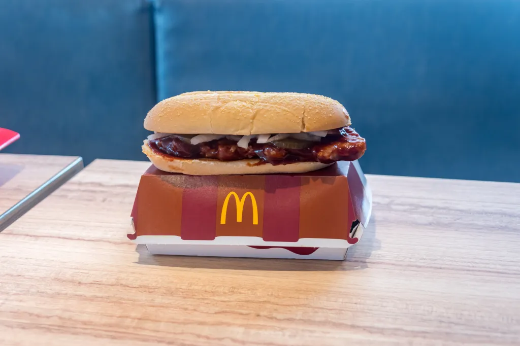 A McDonald's McRib sandwich rests on top of its box on a wooden table.