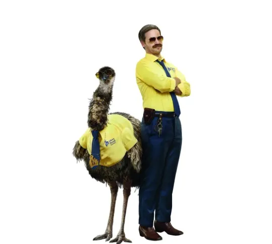 Actor David Hoffman, known as Doug, stands next to the Limu Emu, both wearing matching yellow shirts and sunglasses.