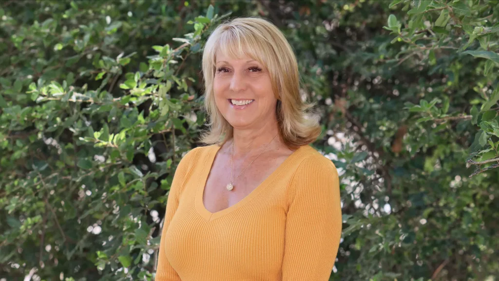 Melanie Richardson in front of a leafy green background.