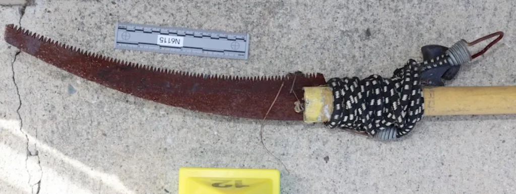 A metal pole with a serrated blade and evidence markers on the ground.