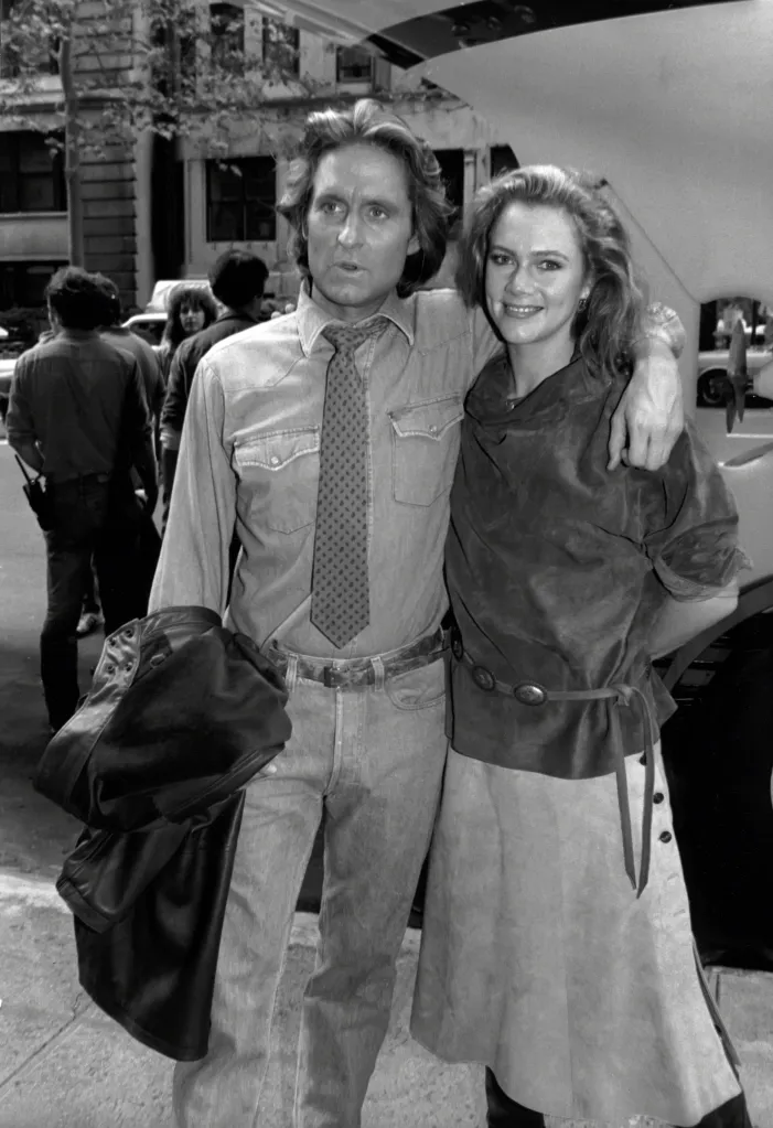 Michael Douglas and Kathleen Turner outdoors with their arms around each other.