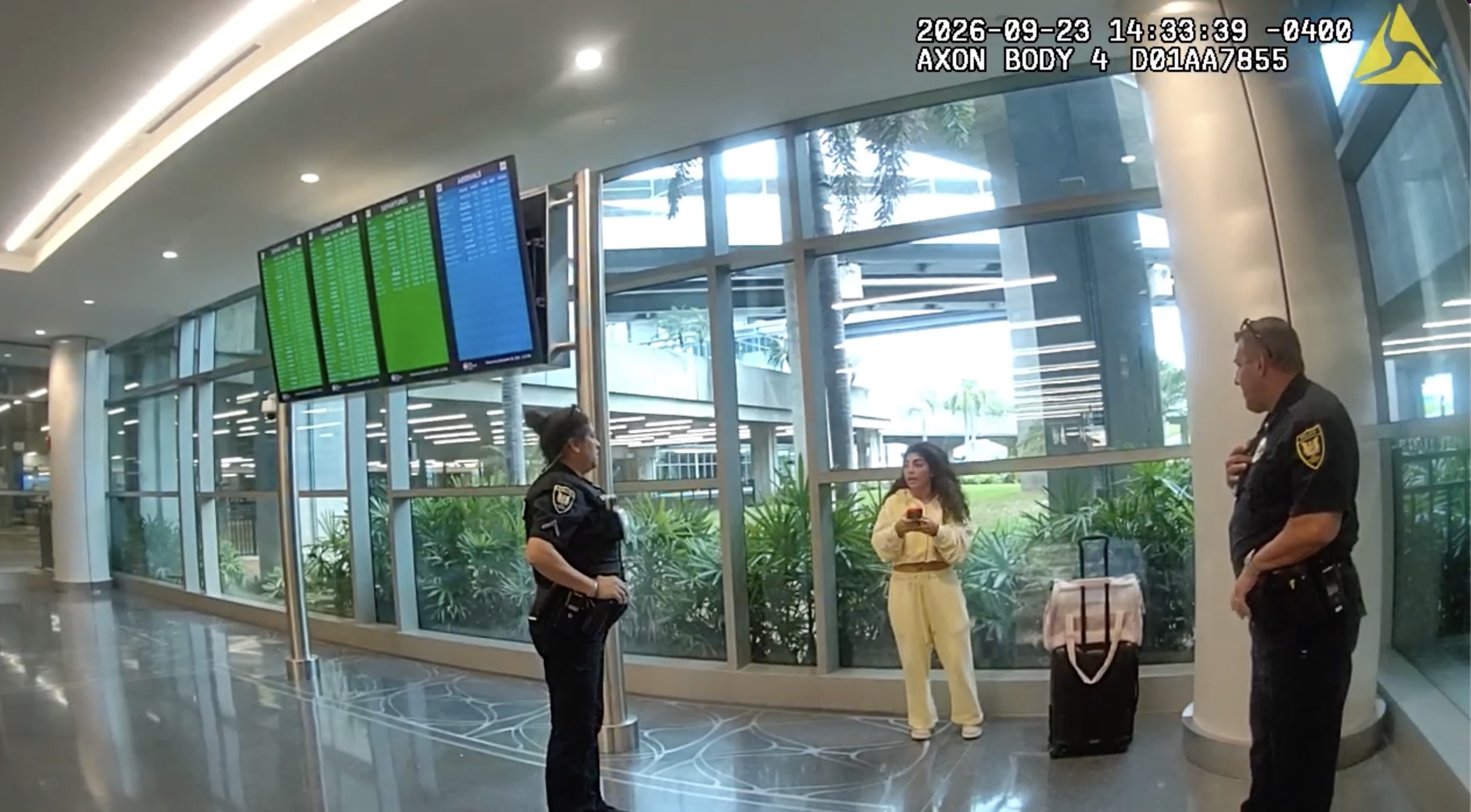 Bodycam footage of Milania Giudice standing near two police officers in an airport terminal.