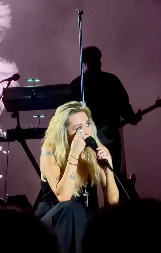 Miley Cyrus crying while holding a microphone on stage.