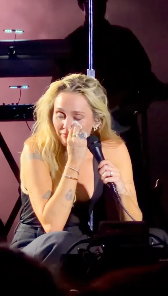 Miley Cyrus crying while holding a microphone on stage.