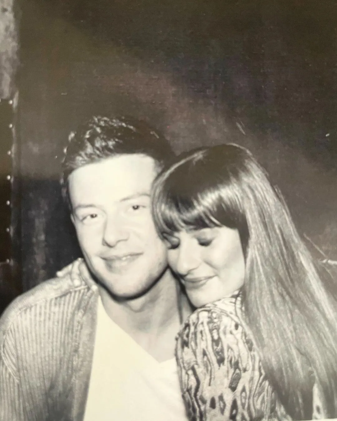 Black-and-white photo of Lea Michele resting her head against Cory Monteith's shoulder and smiling.