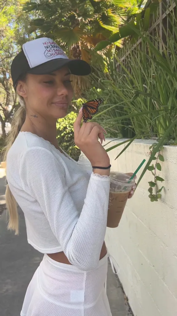 Sahara Ray holding a butterfly on her finger while holding an iced coffee.