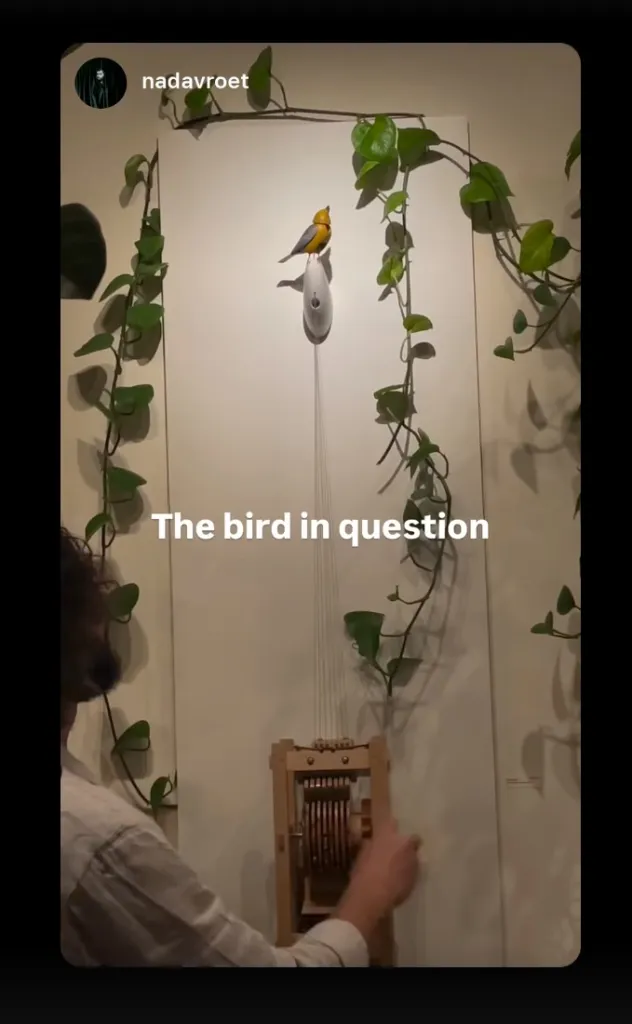 A person operating a mechanical wooden device that controls an animated bird sculpture named Molly.
