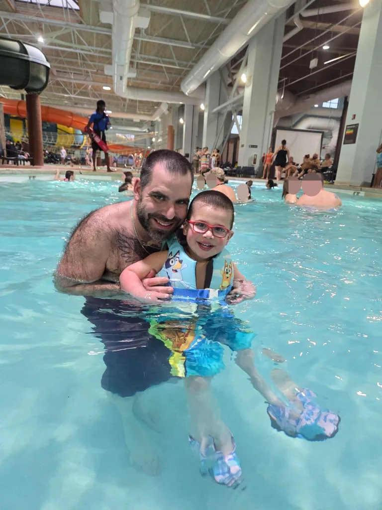 Charles Harrison and his three-year-old son smiling together in a swimming pool at a resort hotel.