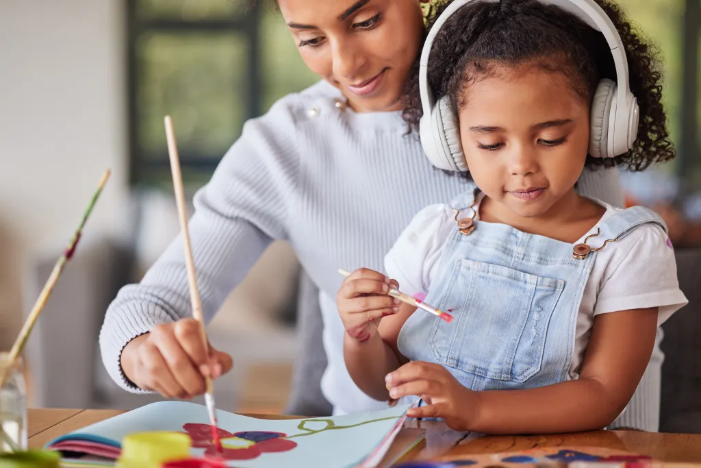 A mother and daughter wearing headphones paint together at home.