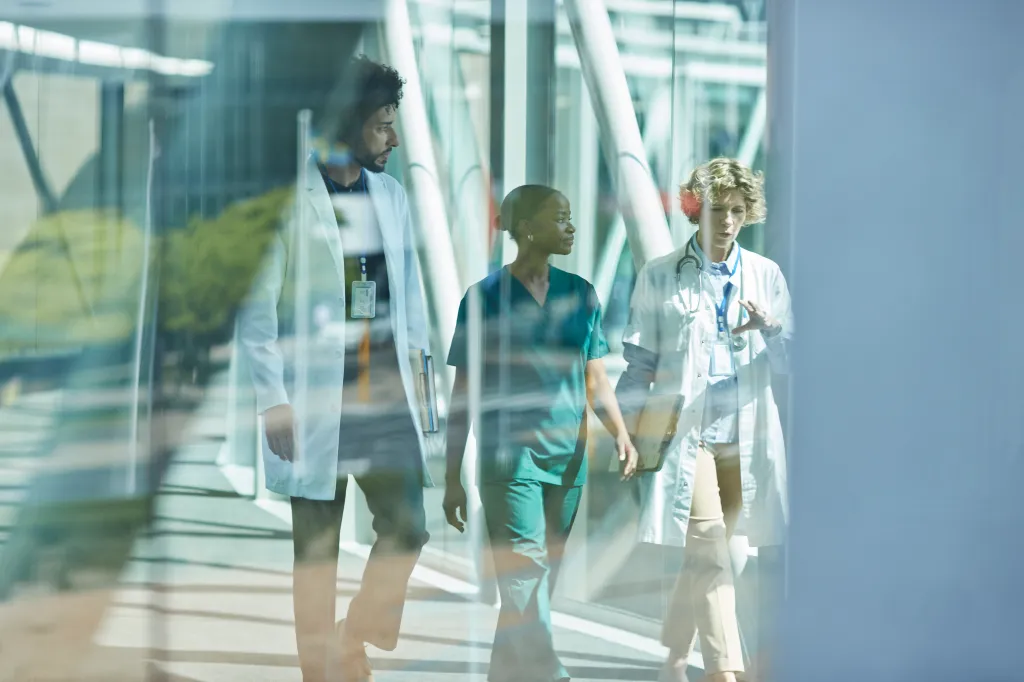 Multiracial medical workers discuss while walking on an elevated walkway.
