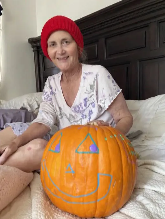 Nadine Jett sitting on a bed with a painted pumpkin.