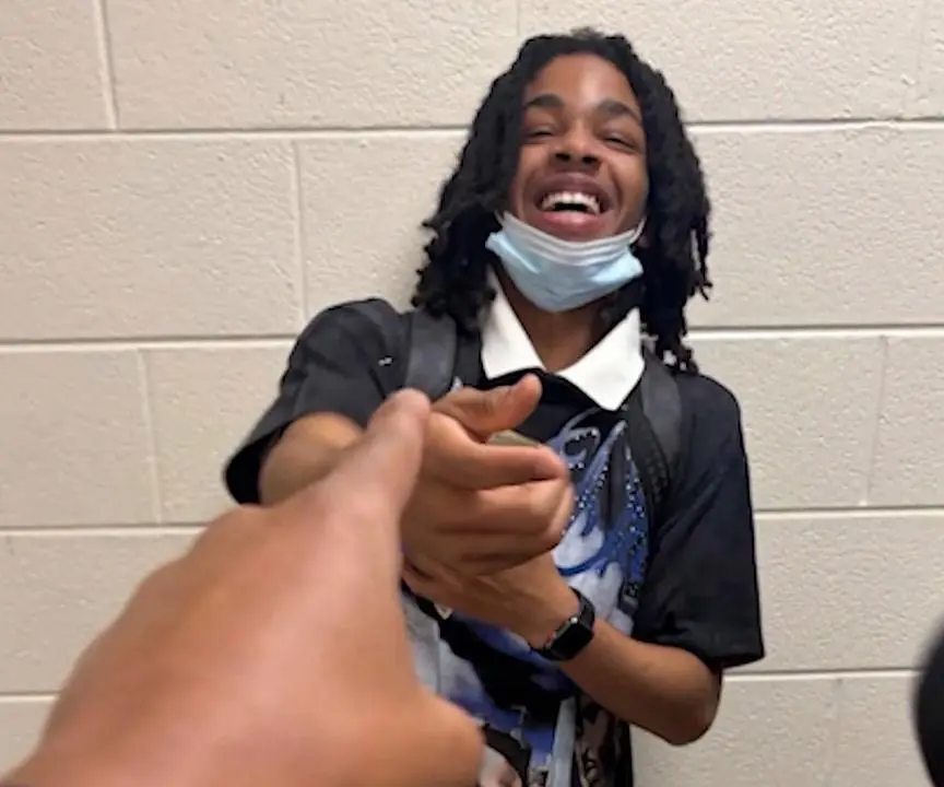 Cameron Frierson smiling while holding money with a face mask under his chin.
