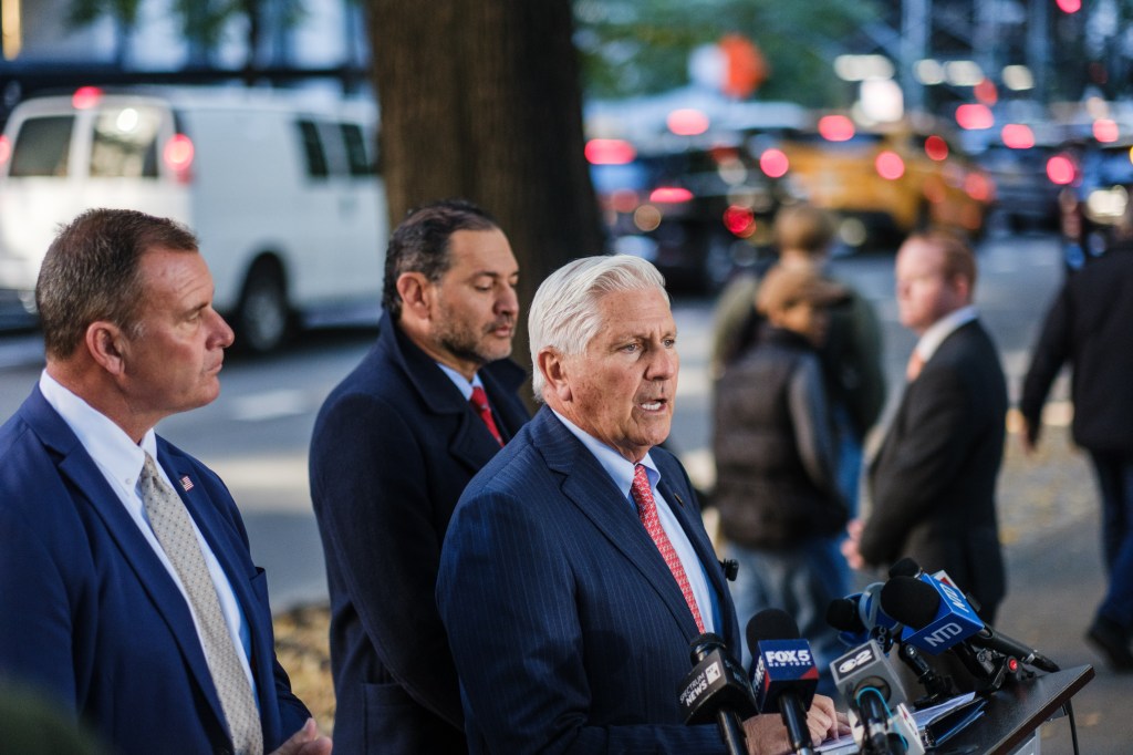 Bruce Blakeman speaks at a campaign event in Manhattan, flanked by supporters and microphones.