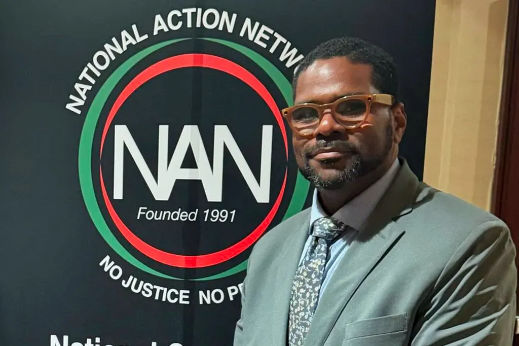 National Action Network Michigan president Rev. Charles E. Williams standing in front of a National Action Network banner.