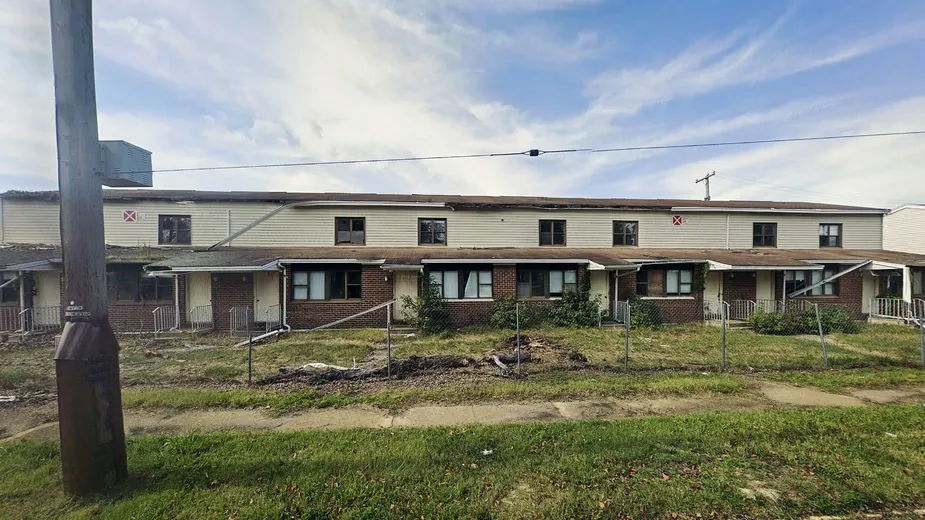 An abandoned, blighted apartment complex with overgrown grass and damaged roofs.