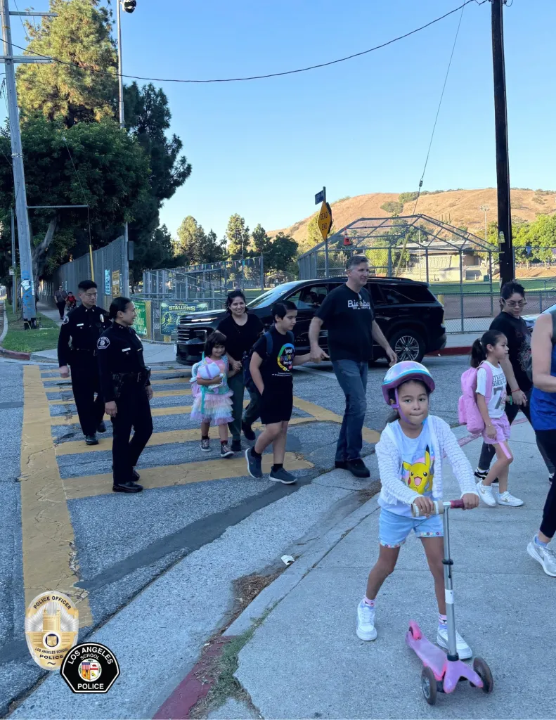 Los Angeles School Police officers walking near children and parents in a crosswalk.