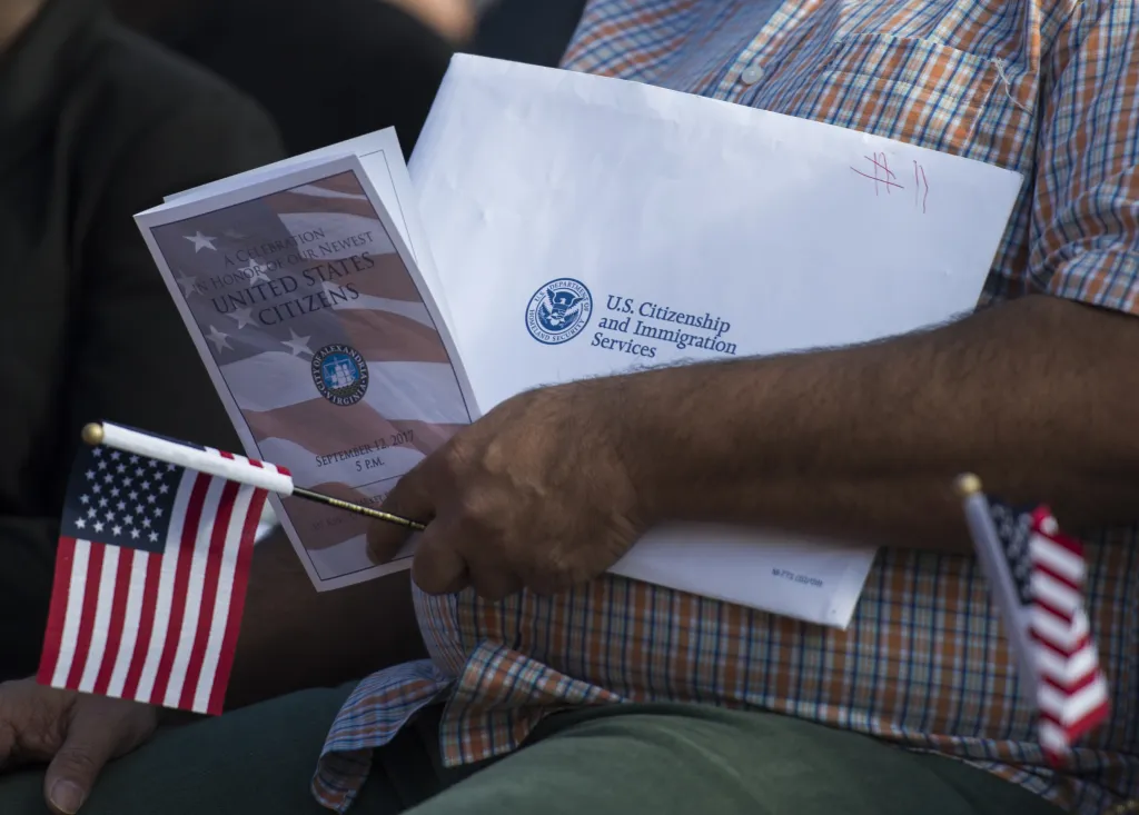 A new U.S. citizen holds a naturalization ceremony information packet and small American flags.