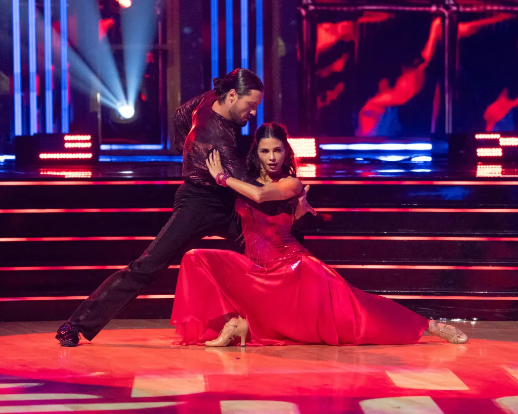 Valentin Chmerkovskiy and Jenna Dewan dance on a stage with red lights.