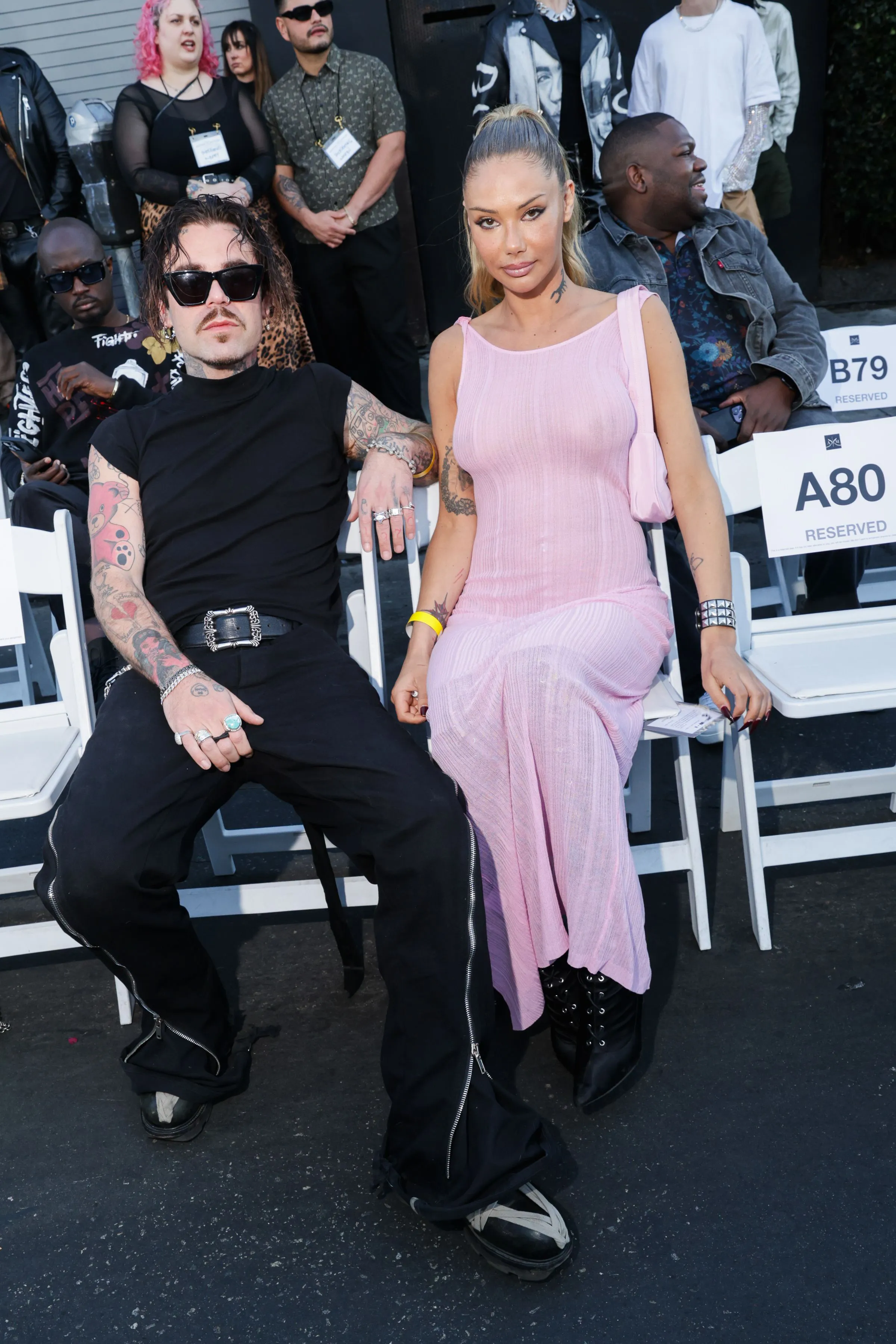 Mod Sun and Sahara Ray sit in reserved white chairs at a fashion event.
