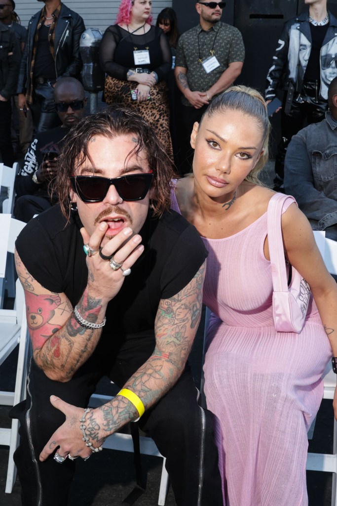 Mod Sun and Sahara Ray pose together, seated, with other attendees visible in the background.