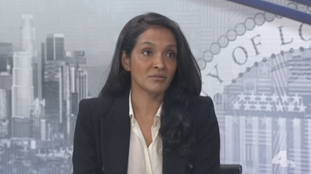 Nithya Raman sitting before a backdrop depicting a city skyline and the seal of Los Angeles.