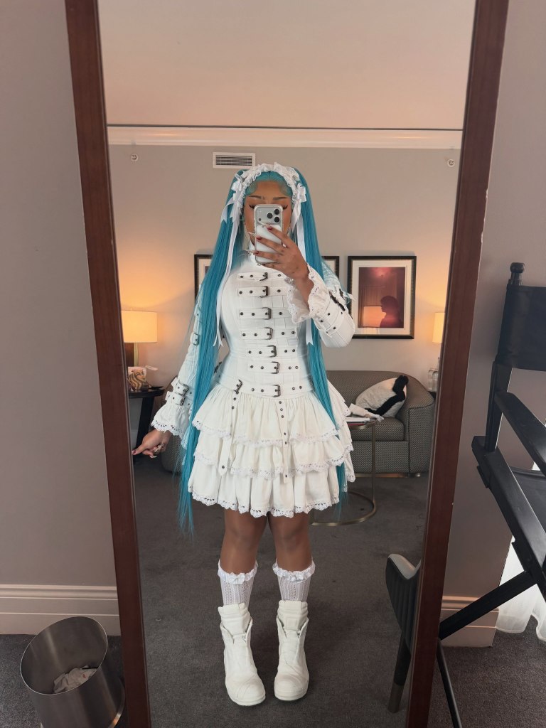 North West poses in a mirror wearing a white, tiered dress and long bright blue hair.