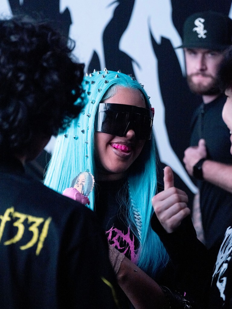 North West with bright blue hair and sunglasses gives a thumbs up while surrounded by fans at a pop-up shop.