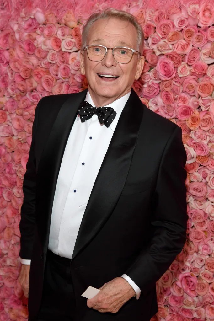 Bob Mackie attends the Met Gala at the Metropolitan Museum of Art in a tuxedo with a polka-dot bow tie in front of a pink floral wall.