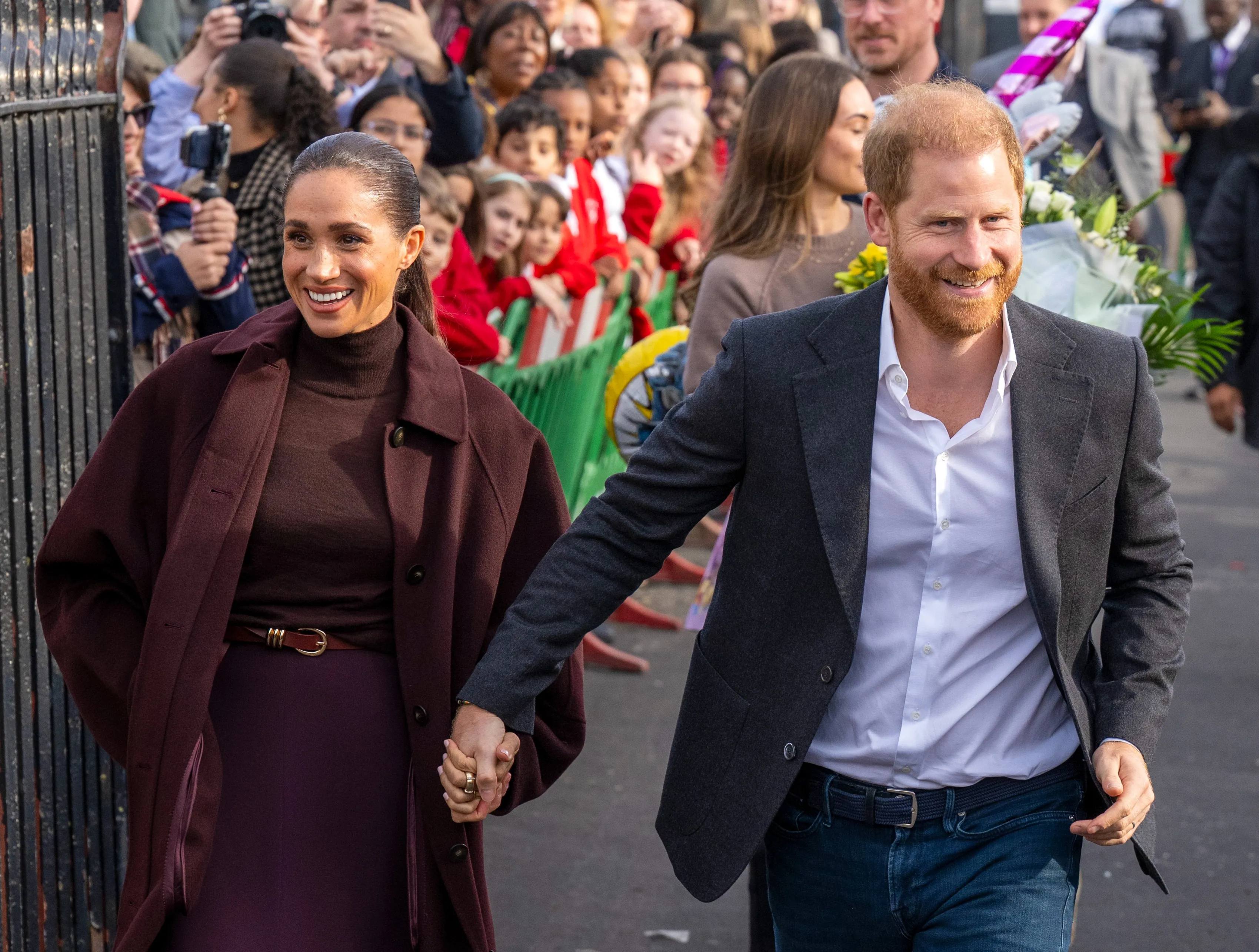 Prince Harry and Meghan Markle holding hands while smiling as they walk past a crowd in Nottingham.
