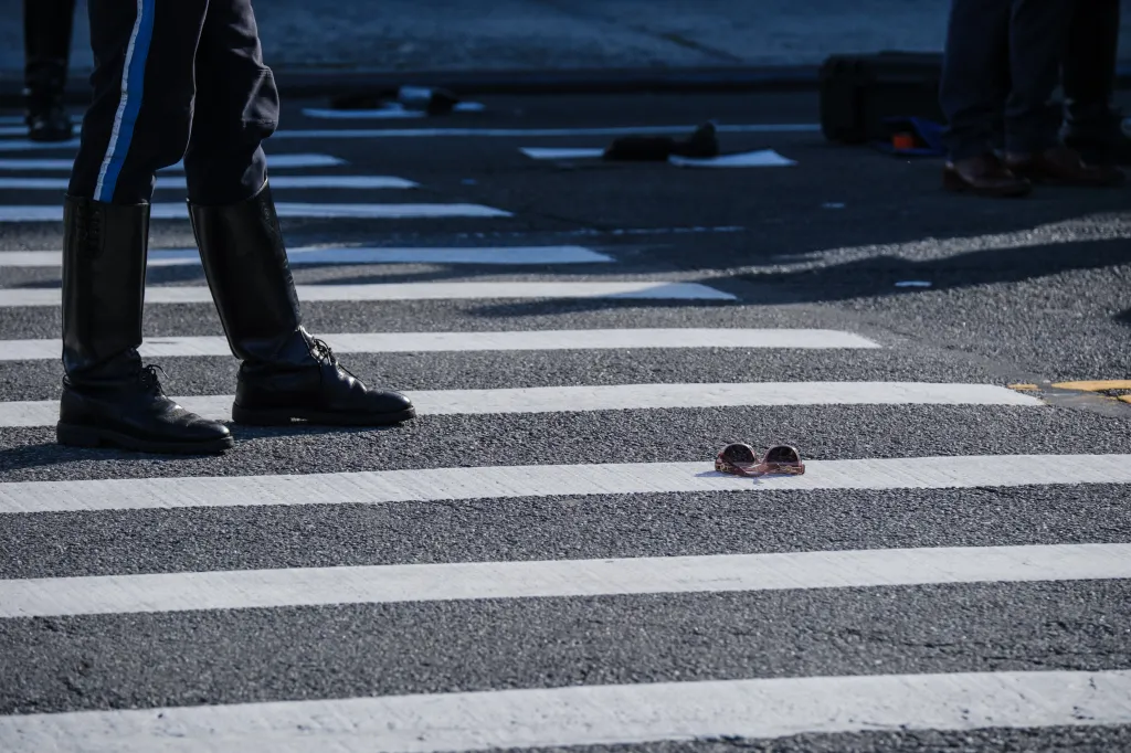 A pair of sunglasses lies in a crosswalk near a police officer's boots at the scene of a crash.
