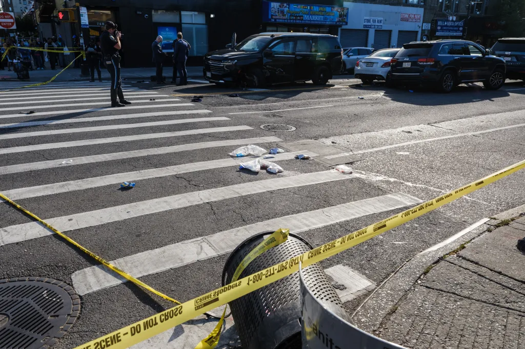 New York City Police Department officers stand at the scene of a multiple vehicle crash with yellow police tape surrounding the area.