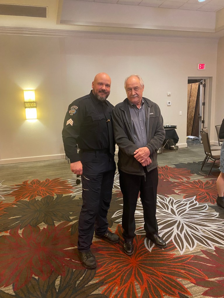 Officer Aaron Zaliponi standing with another man in a room with a patterned carpet.