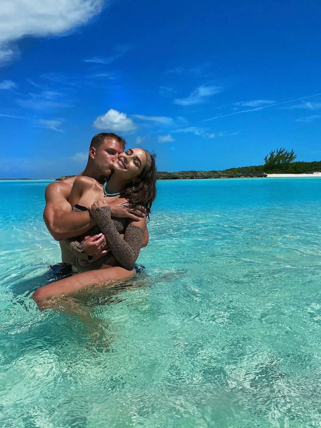 Olivia Culpo and Christian McCaffrey embrace in clear blue water.