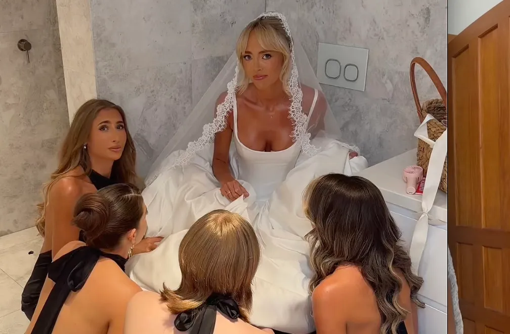 Annie Knight in a white wedding gown, sitting on the floor surrounded by her bridesmaids in a bathroom.