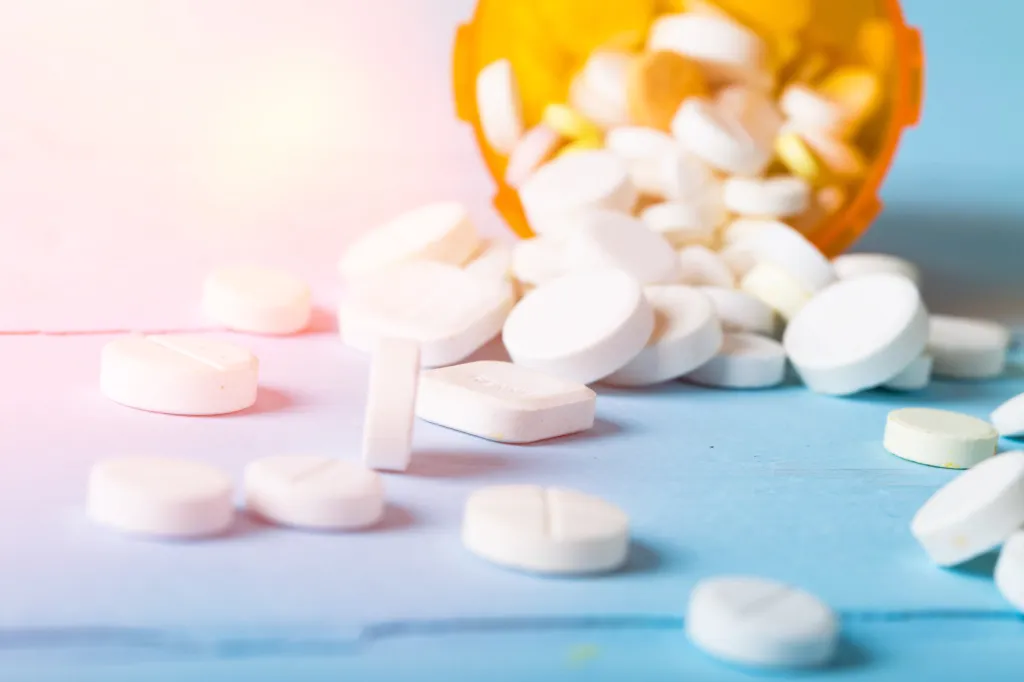 Prescription pills spilled from an orange medication bottle.