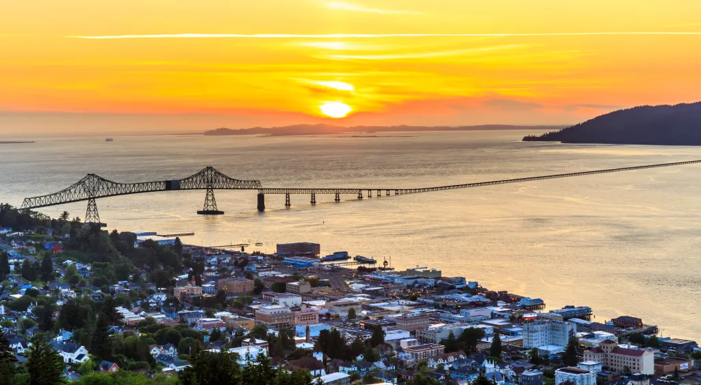 High-angle view of Astoria, Oregon, at sunset, showing the Columbia River and the Astoria-Megler Bridge.