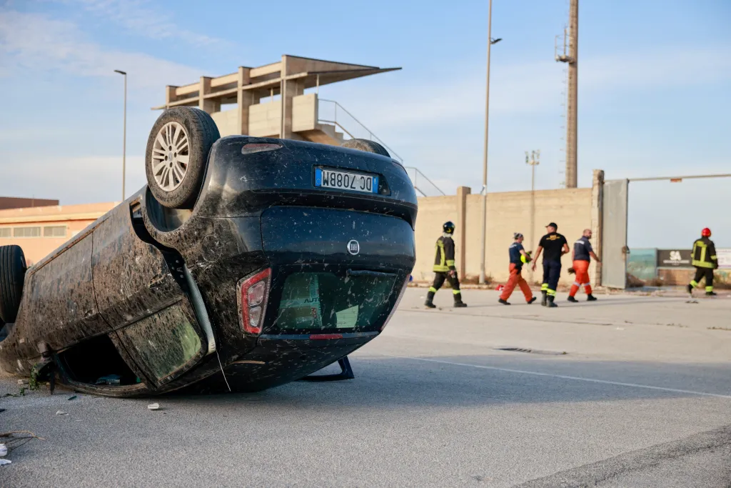 An overturned car lies on a road with emergency workers in the background after a tornado struck Petrosino, Sicily.