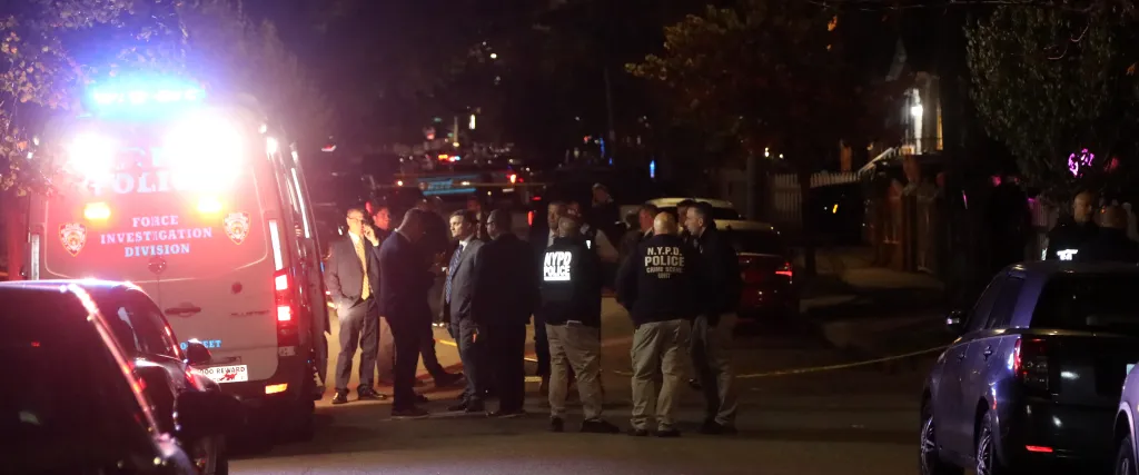 Police officers and investigators gather at a shooting scene on a residential street at night, with an NYPD Force Investigation Division vehicle parked nearby.