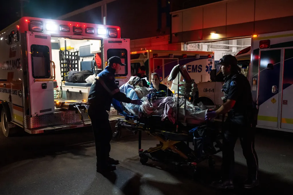Paramedics load an injured person into an ambulance at night outside a health center.