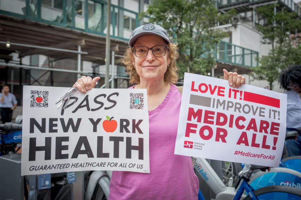 A participant holds two signs at a healthcare protest in Manhattan, New York.