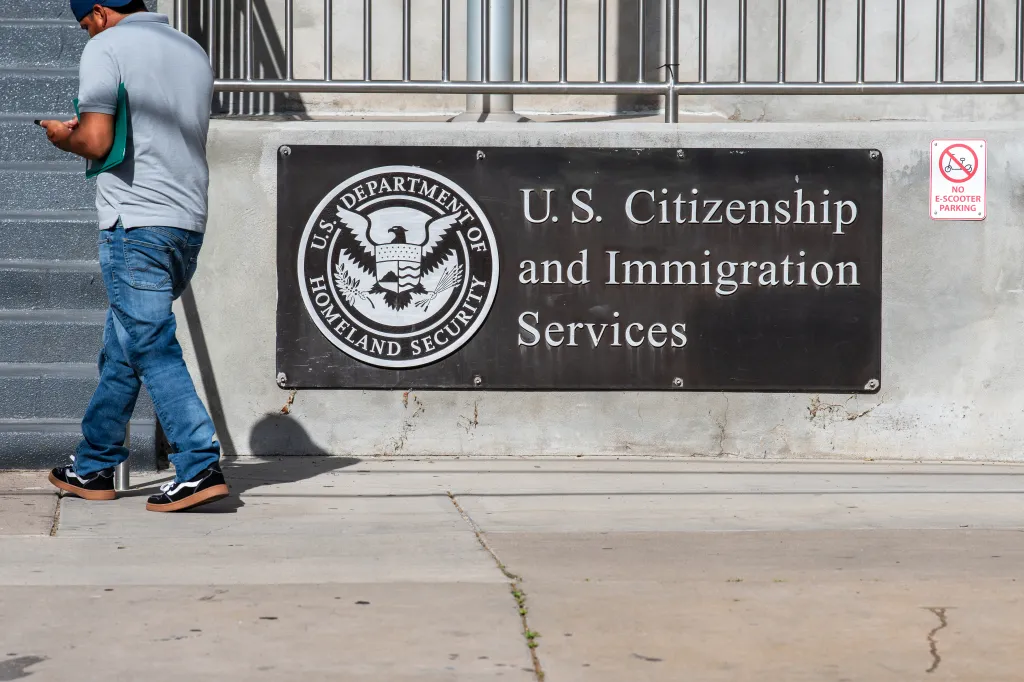 A pedestrian walks past the exterior sign and seal of the U.S. Citizenship and Immigration Services field office.