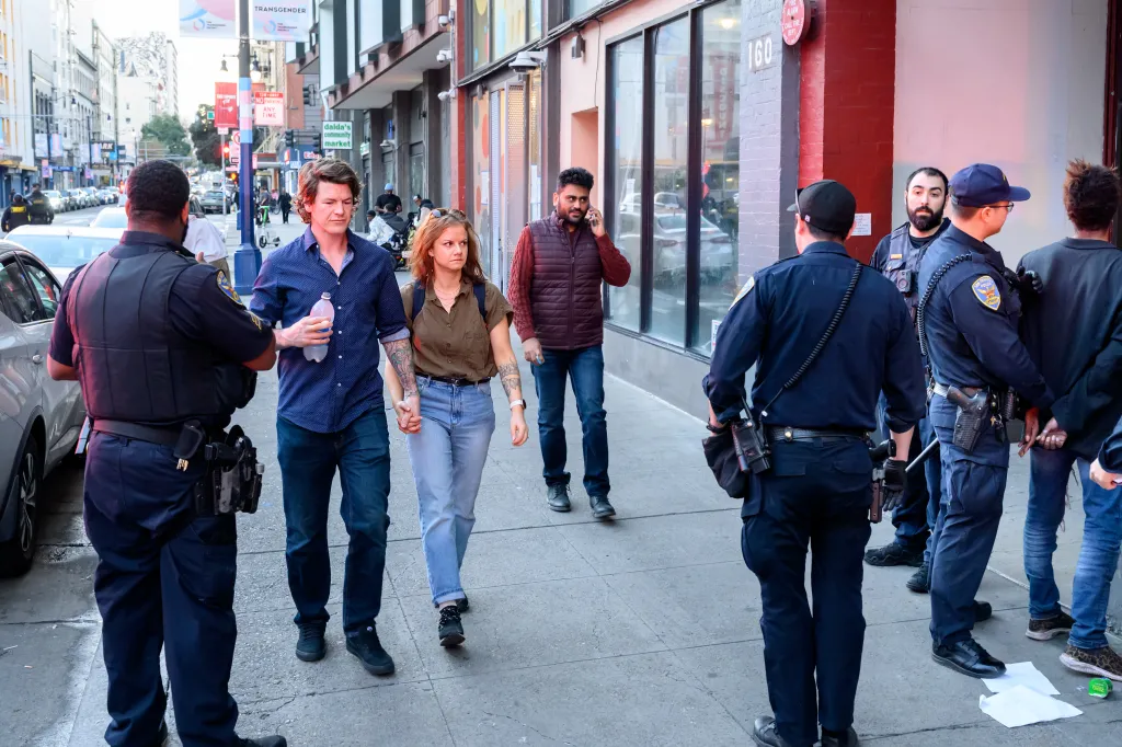 Pedestrians pass police officers as they detain a man in San Francisco's Tenderloin neighborhood.
