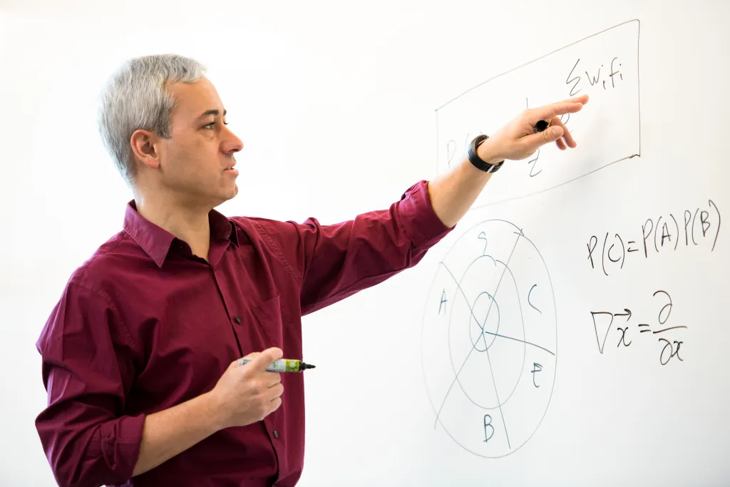 Pedro Domingos pointing at a whiteboard with formulas and diagrams.