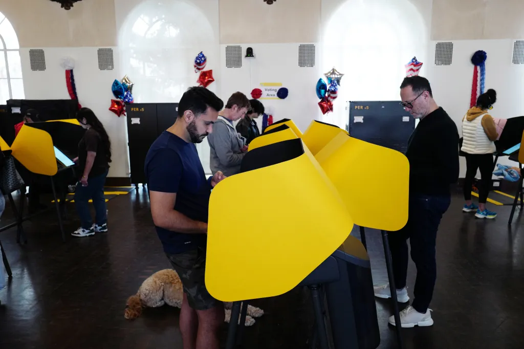 People casting their votes at yellow voting booths inside a room.