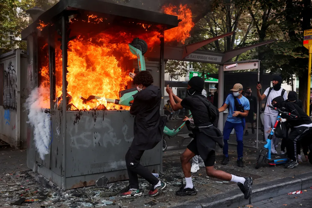 People attempt to put an electric scooter into a burning structure on a street during a protest in Liege.