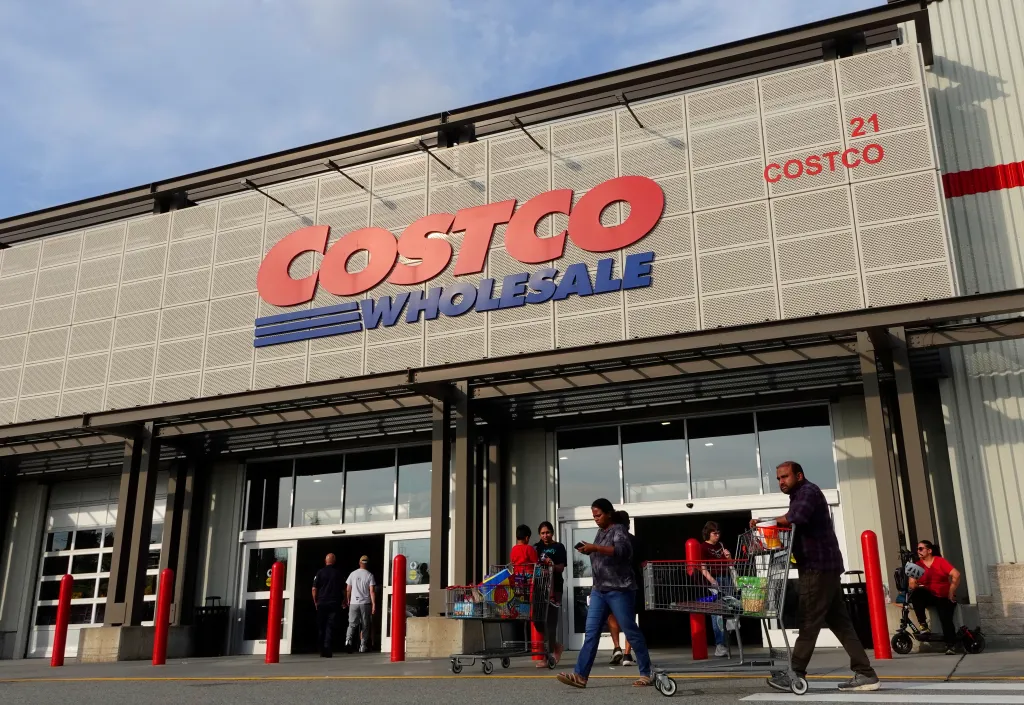 People walk out of a Costco Wholesale store with a shopping cart of goods.